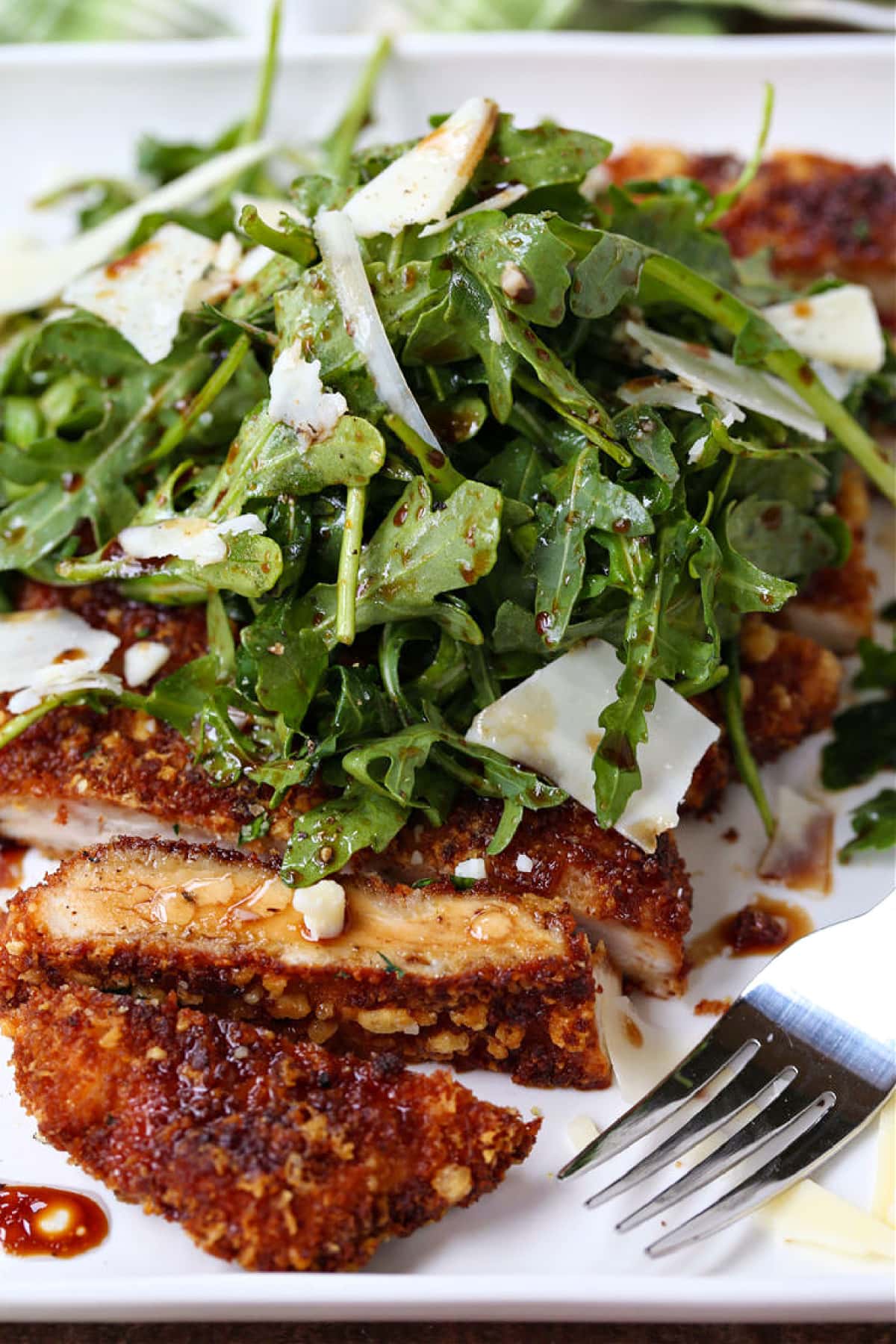 sliced chicken cutlet on a plate with arugula and parmesan cheese