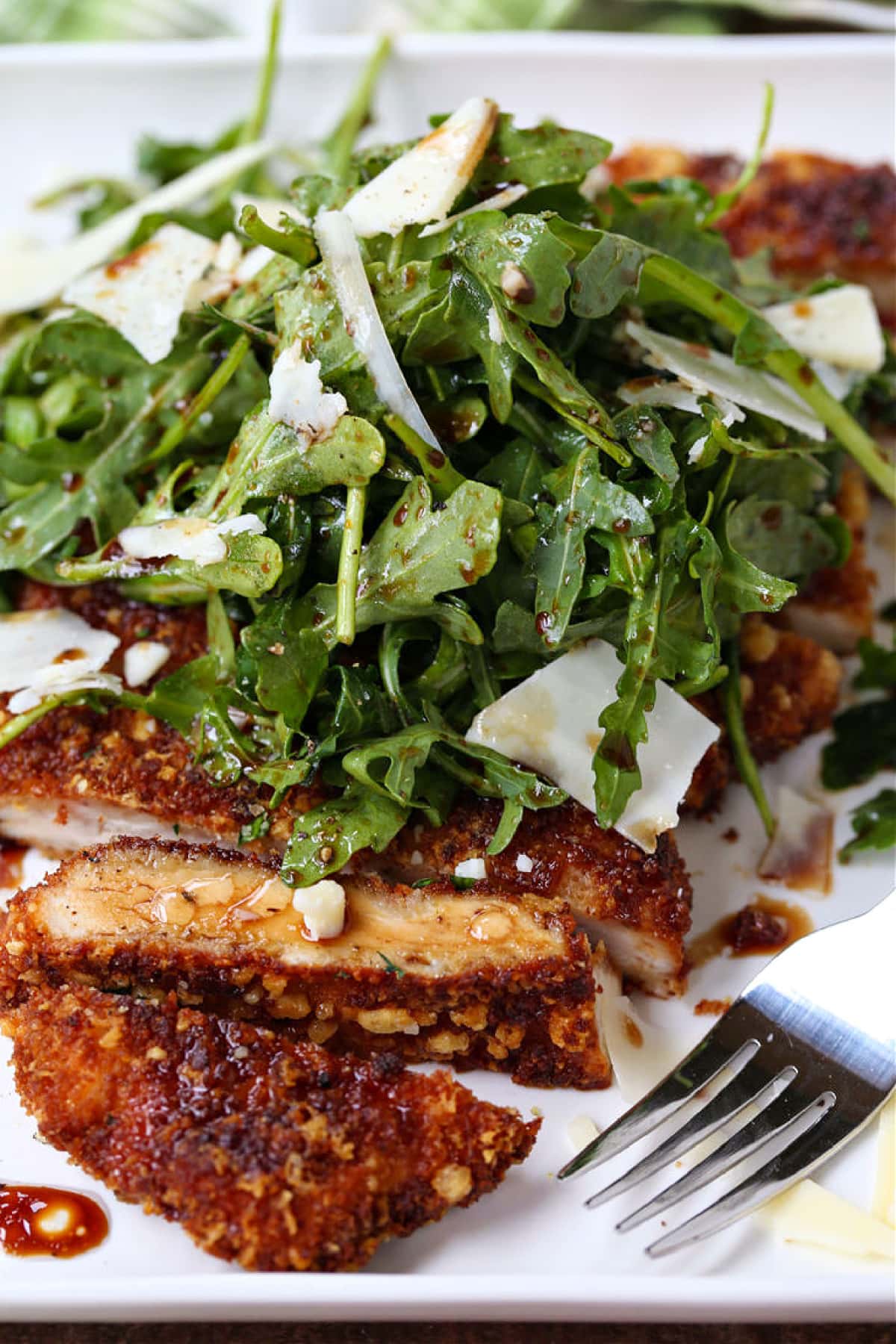 Chicken Milanese is an easy, restaurant quality dish that's ready in just 30 minutes! Warm chicken cutlets topped with a crisp arugula salad! sliced chicken cutlet on a plate with arugula and parmesan cheese