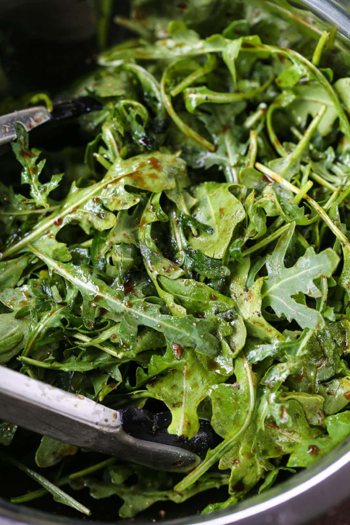 arugula in a bowl with tongs