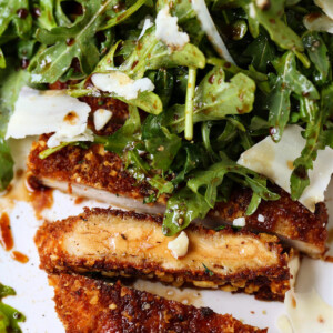 chicken cutlet sliced on a plate with arugula salad