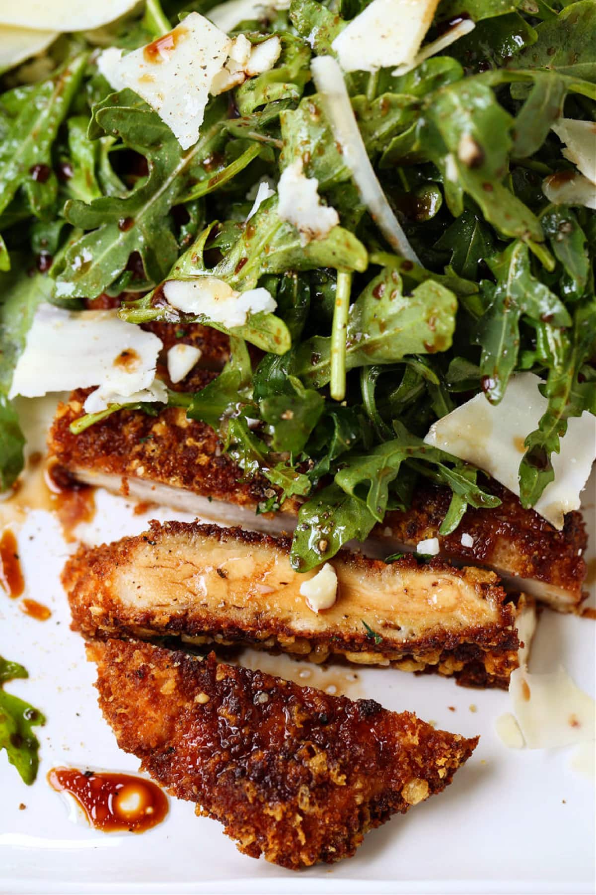 Chicken Milanese is an easy, restaurant quality dish that's ready in just 30 minutes! Warm chicken cutlets topped with a crisp arugula salad! chicken cutlet sliced on a plate with arugula salad