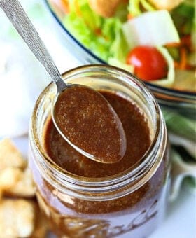 a spoon of balsamic dressing over jar with salad in background