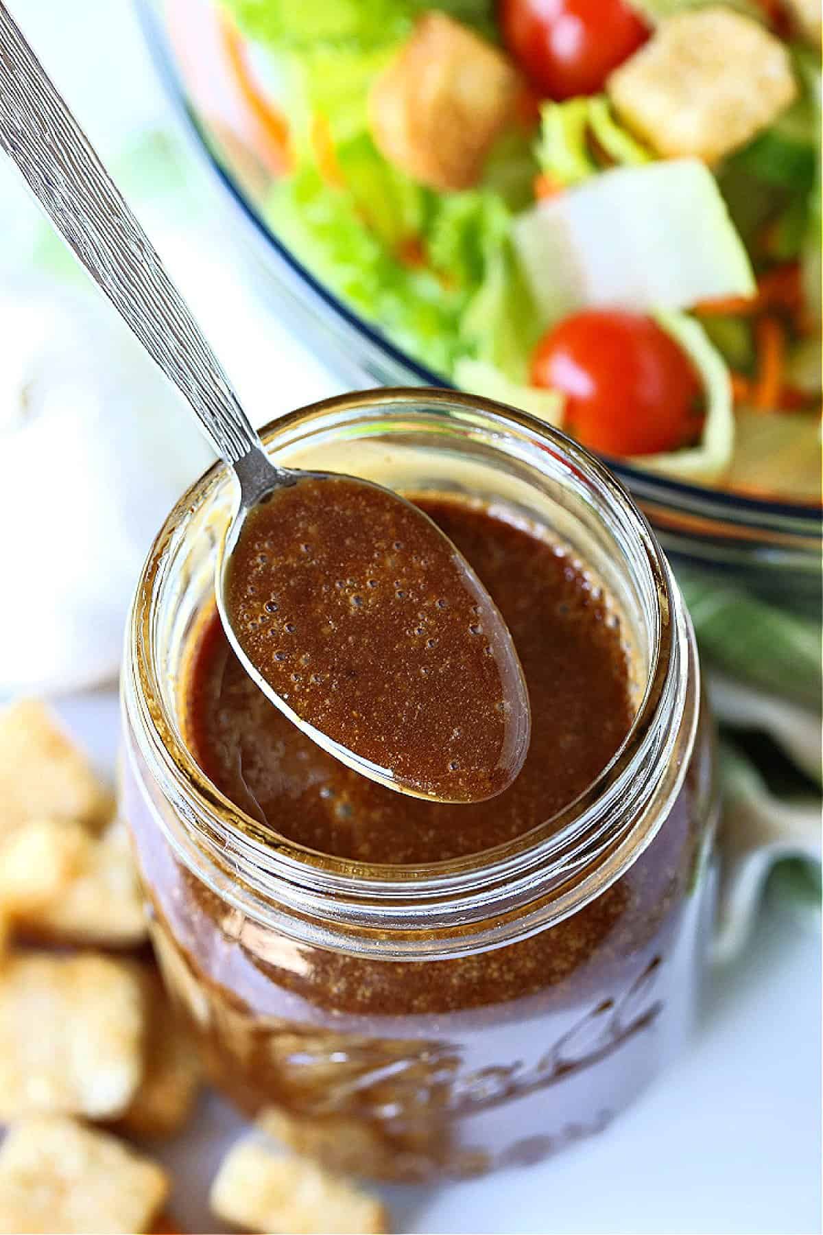 a spoon of balsamic dressing over jar with salad in background
