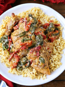 Chicken breast with sun dried tomato and spinach cream sauce served over a bed of couscous on a plate.