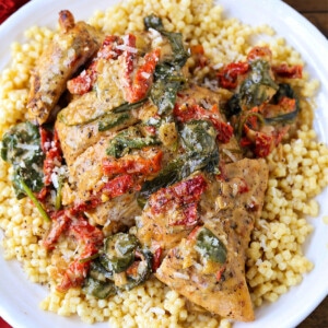 Chicken breast with sun dried tomato and spinach cream sauce served over a bed of couscous on a plate.