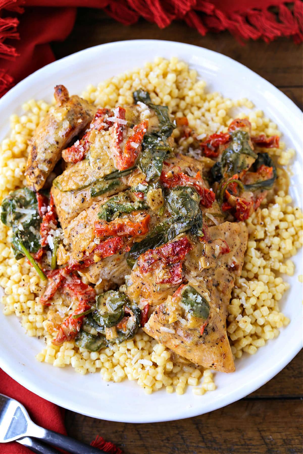 Chicken breast with sun dried tomato and spinach cream sauce served over a bed of couscous on a plate.