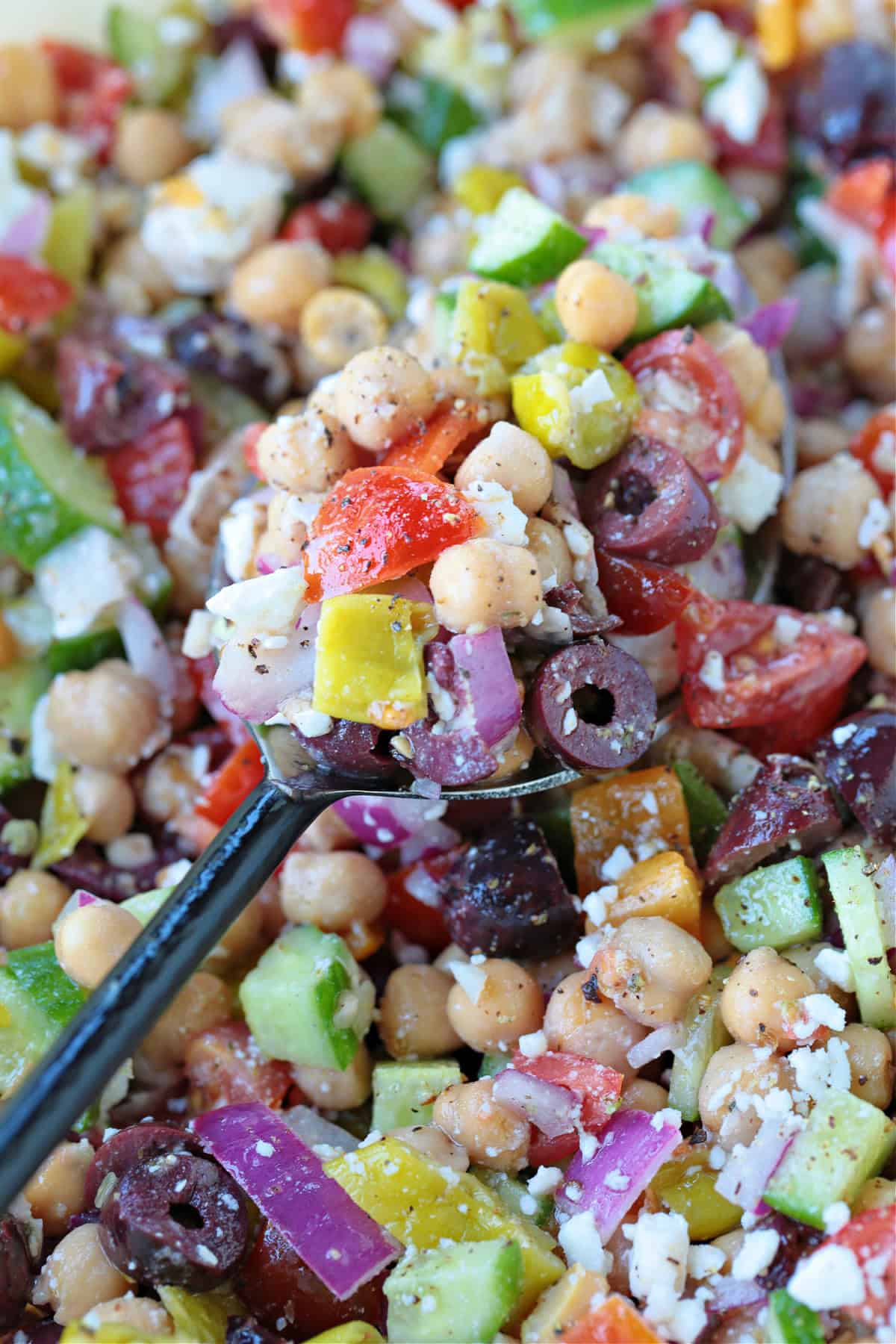 Greek Chickpea Salad is a taste-bud sensation! Loaded with crunchy vegetables, chickpeas and feta cheese tossed in a red wine vinaigrette. chickpea salad with greek flavors on spoon