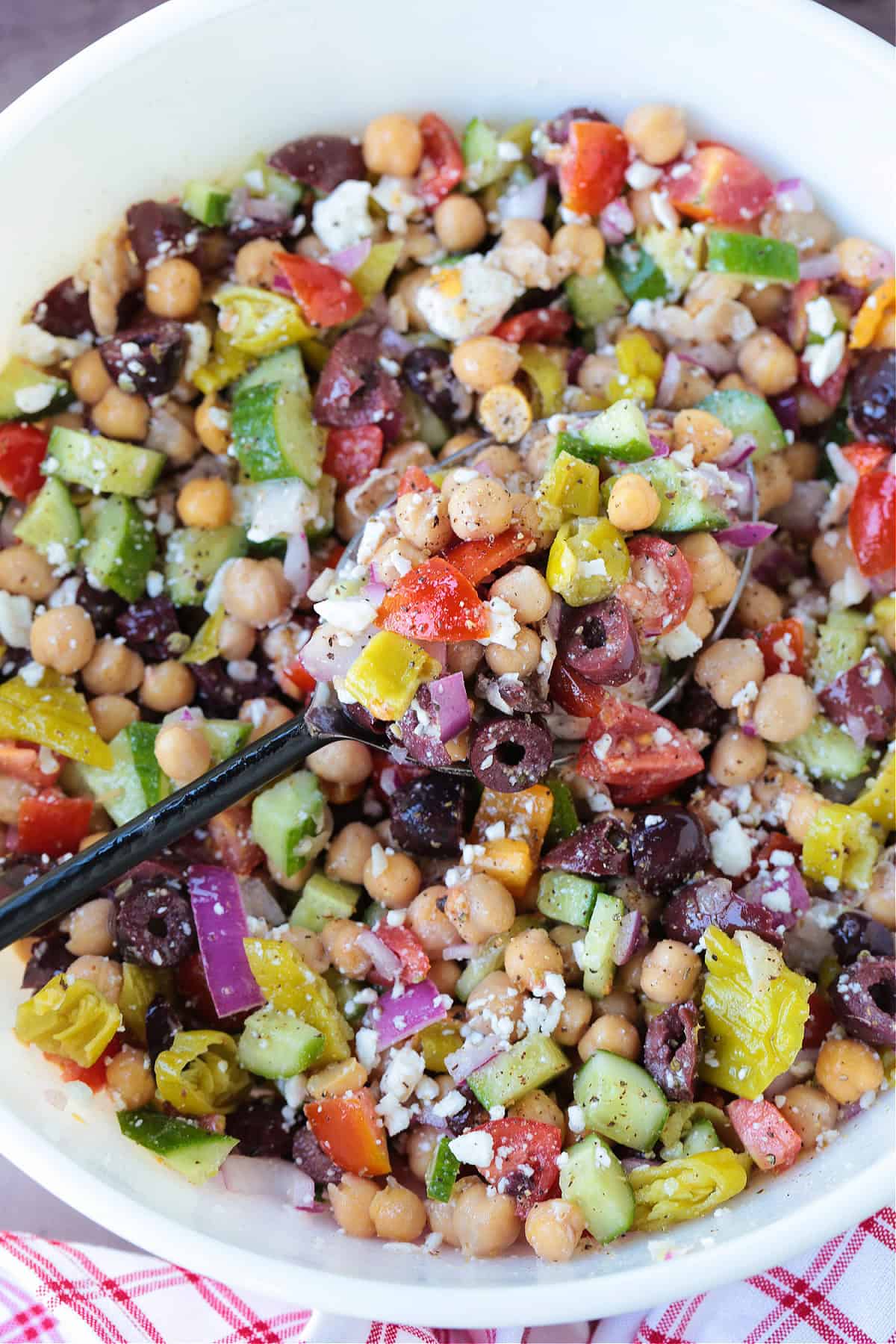 Greek Chickpea Salad is a taste-bud sensation! Loaded with crunchy vegetables, chickpeas and feta cheese tossed in a red wine vinaigrette. greek chickpea salad in a bowl with a spoon