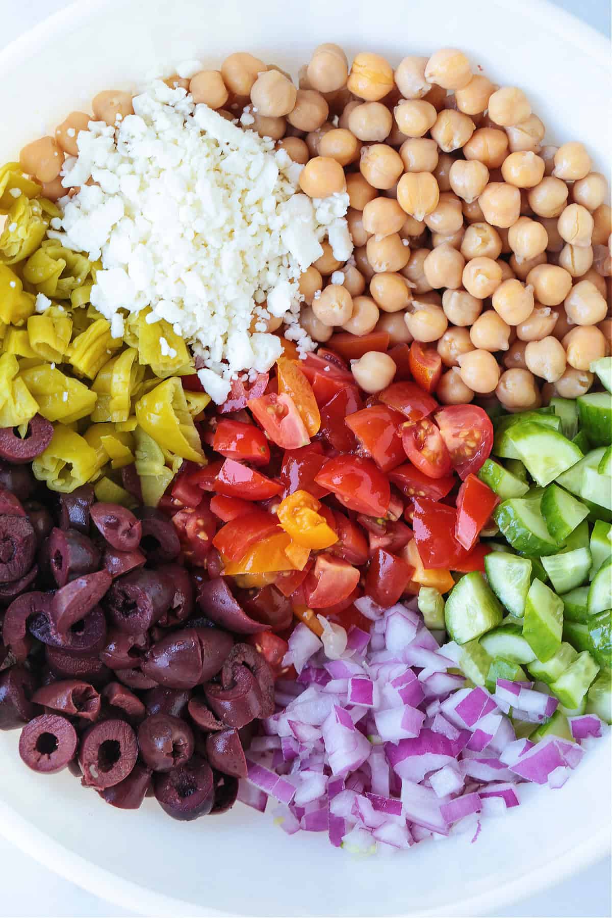 Greek Chickpea Salad is a taste-bud sensation! Loaded with crunchy vegetables, chickpeas and feta cheese tossed in a red wine vinaigrette. chopped vegetables and chickpeas in a white bowl