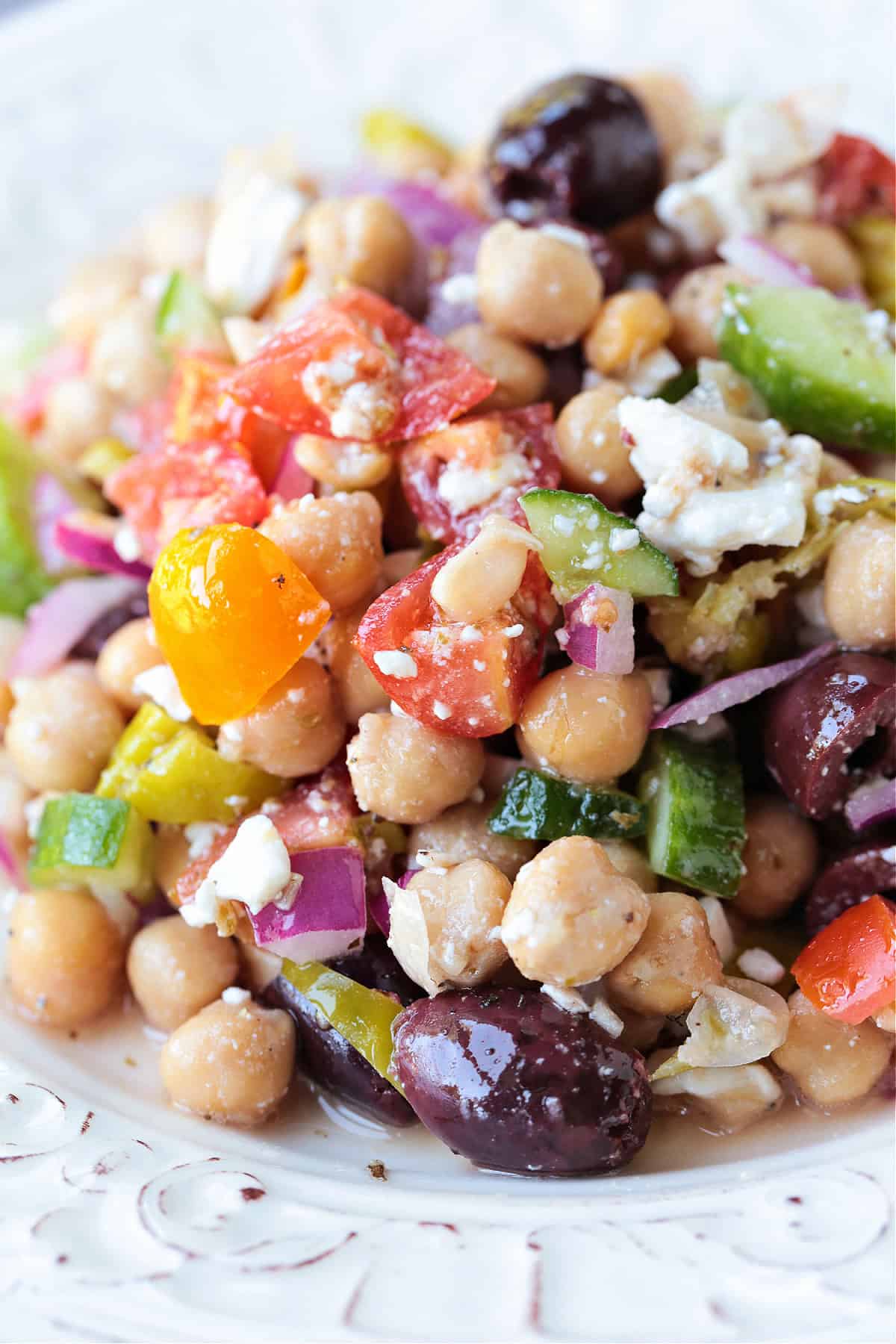 Greek Chickpea Salad is a taste-bud sensation! Loaded with crunchy vegetables, chickpeas and feta cheese tossed in a red wine vinaigrette. chickpea salad with vegetables on a white plate