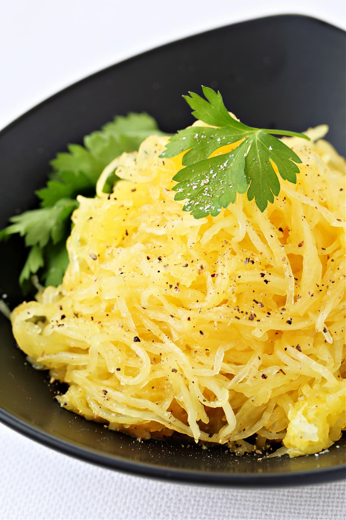 mound of spaghetti squash on black plate with parsley