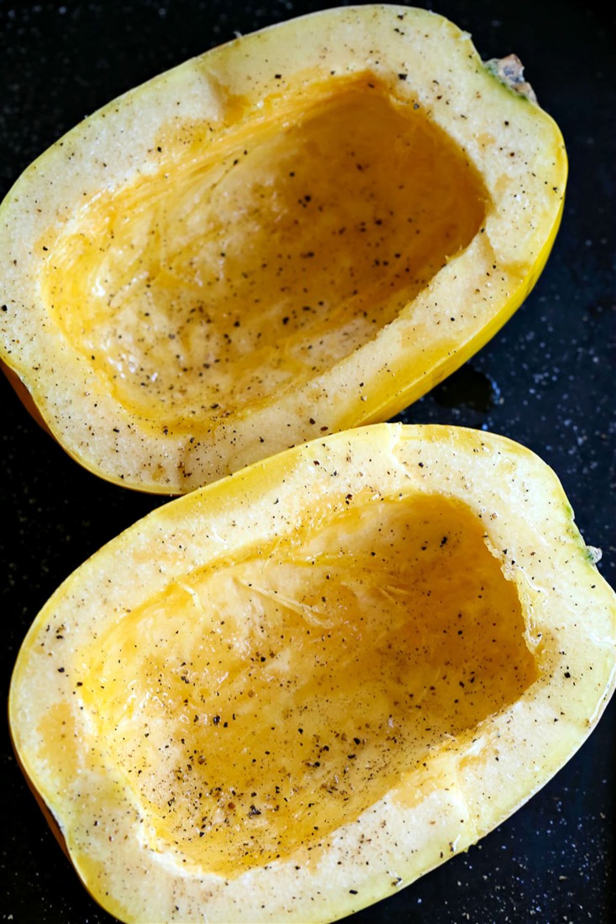 raw spaghetti squash cut in half on baking sheet