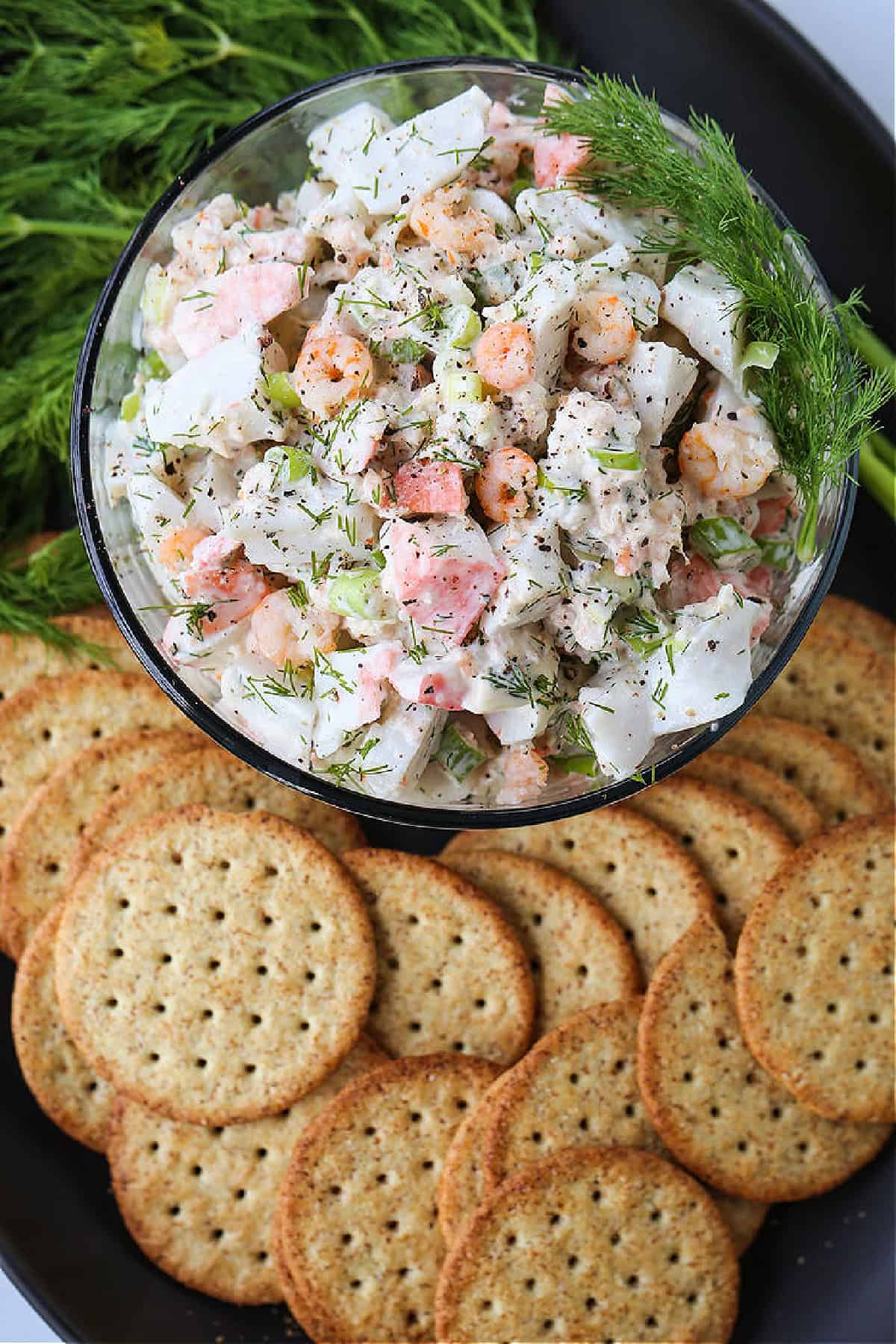 Creamy Seafood Salad is so delicious piled onto crackers or on a roll! An easy seafood appetizer that's perfect for parties and holidays! cold seafood salad in bowl with fresh dill and crackers