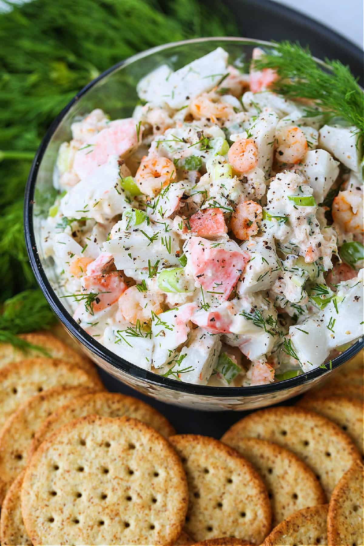 Creamy Seafood Salad is so delicious piled onto crackers or on a roll! An easy seafood appetizer that's perfect for parties and holidays! seafood salad in a glass bowl with crackers