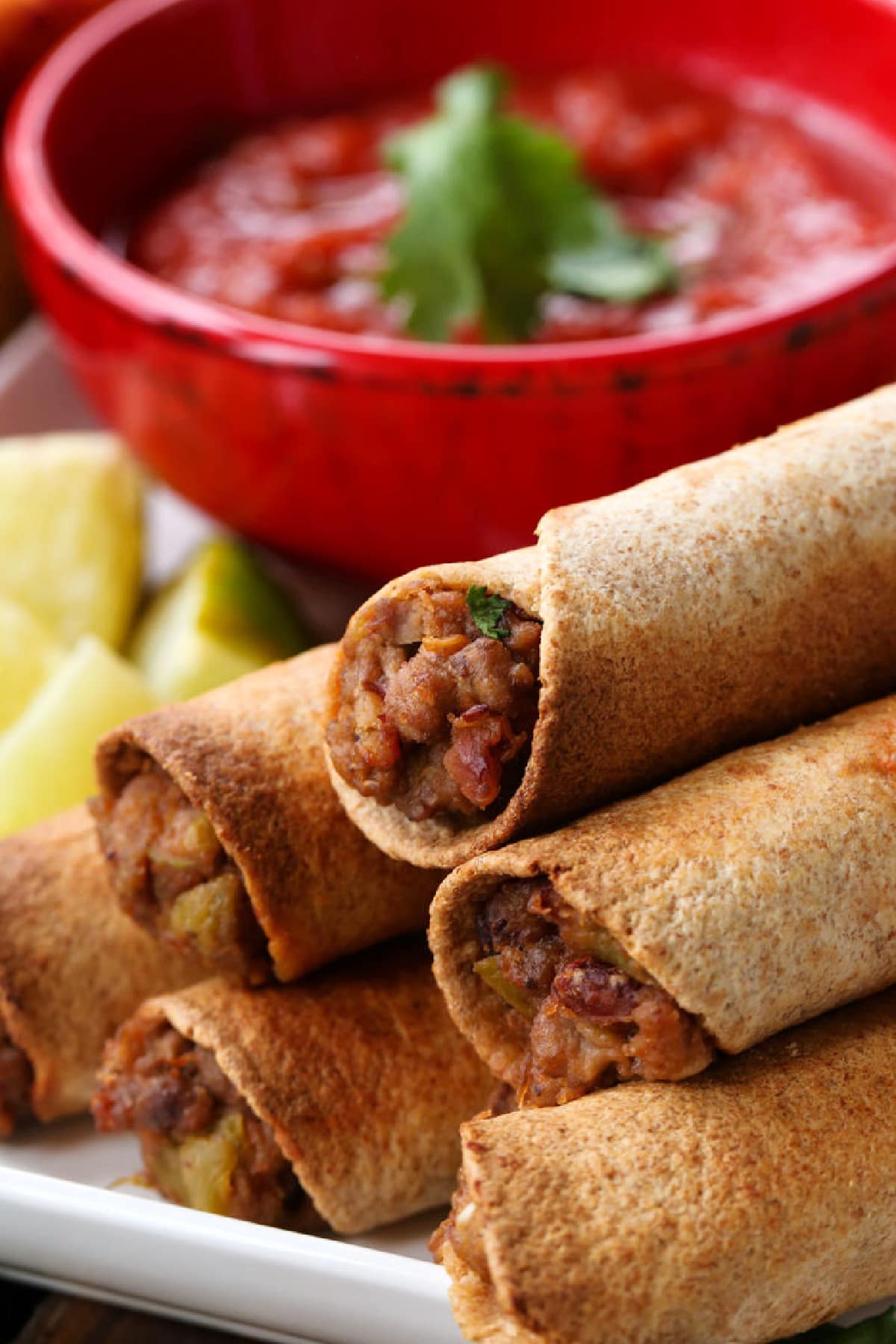 beef taquitos stacked on a plate with salsa