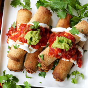 beef taquitos on a plate with salsa and guacamole