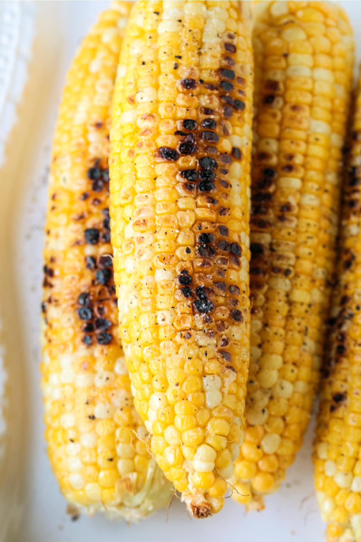 Corn on the Cob on the Grill is an easy and delicious way to make corn! Sweet corn with a charred flavor that makes the perfect summer side! grilled corn on the cob on white platter