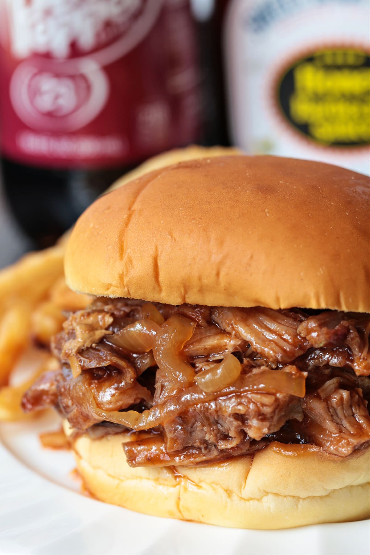Dr. Pepper Pulled Pork is sweet, savory and crazy delicious. Classic cherry soda caramelizes and tenderizes this addicting slow cooker pork! dr. pepper pulled pork sandwich on plate with soda in background