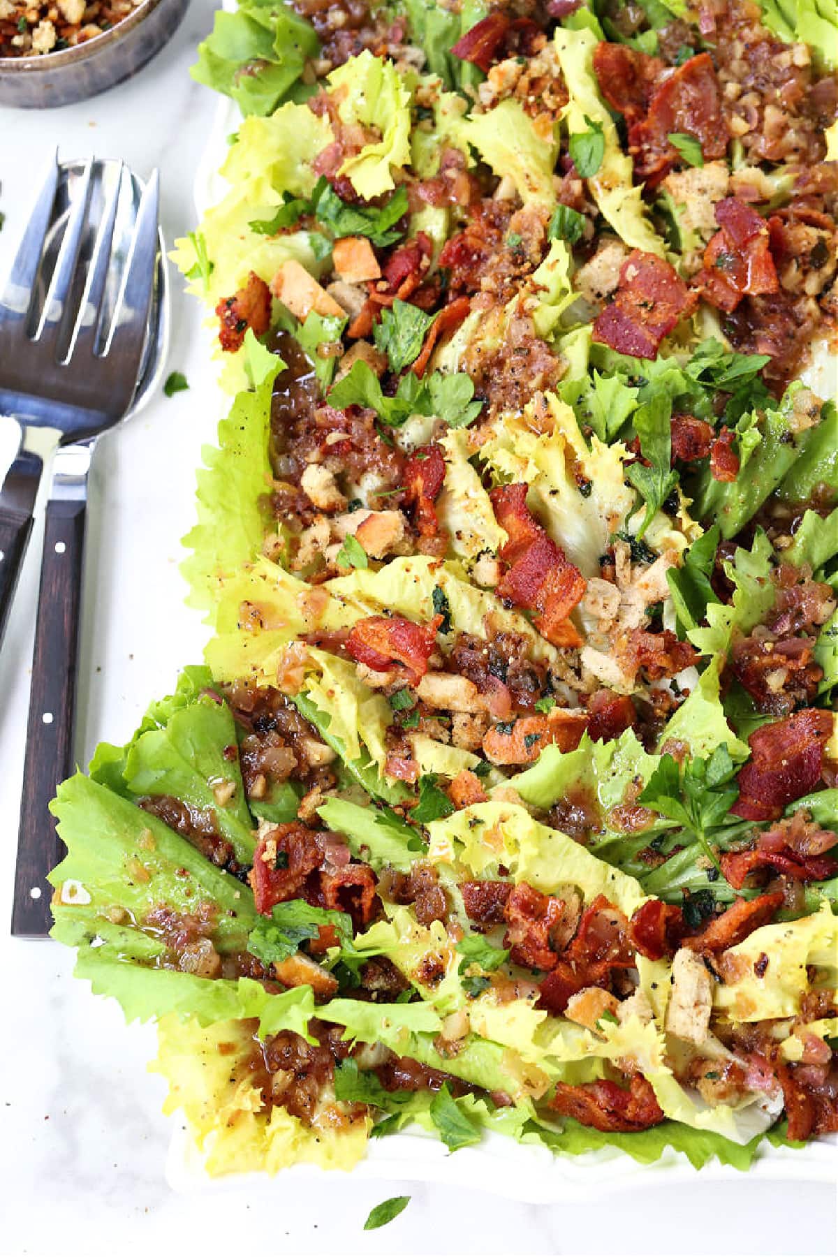 This Escarole Salad Recipe always gets rave reviews! Slightly bitter greens tossed with buttery croutons and a warm bacon dressing. escarole salad on white platter with forks