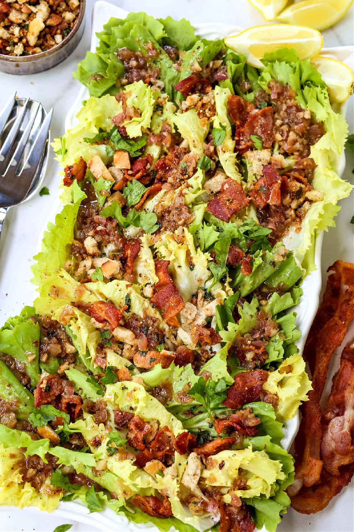 This Escarole Salad Recipe always gets rave reviews! Slightly bitter greens tossed with buttery croutons and a warm bacon dressing. escarole salad with bacon and breadcrumbs on platter with fork on the side