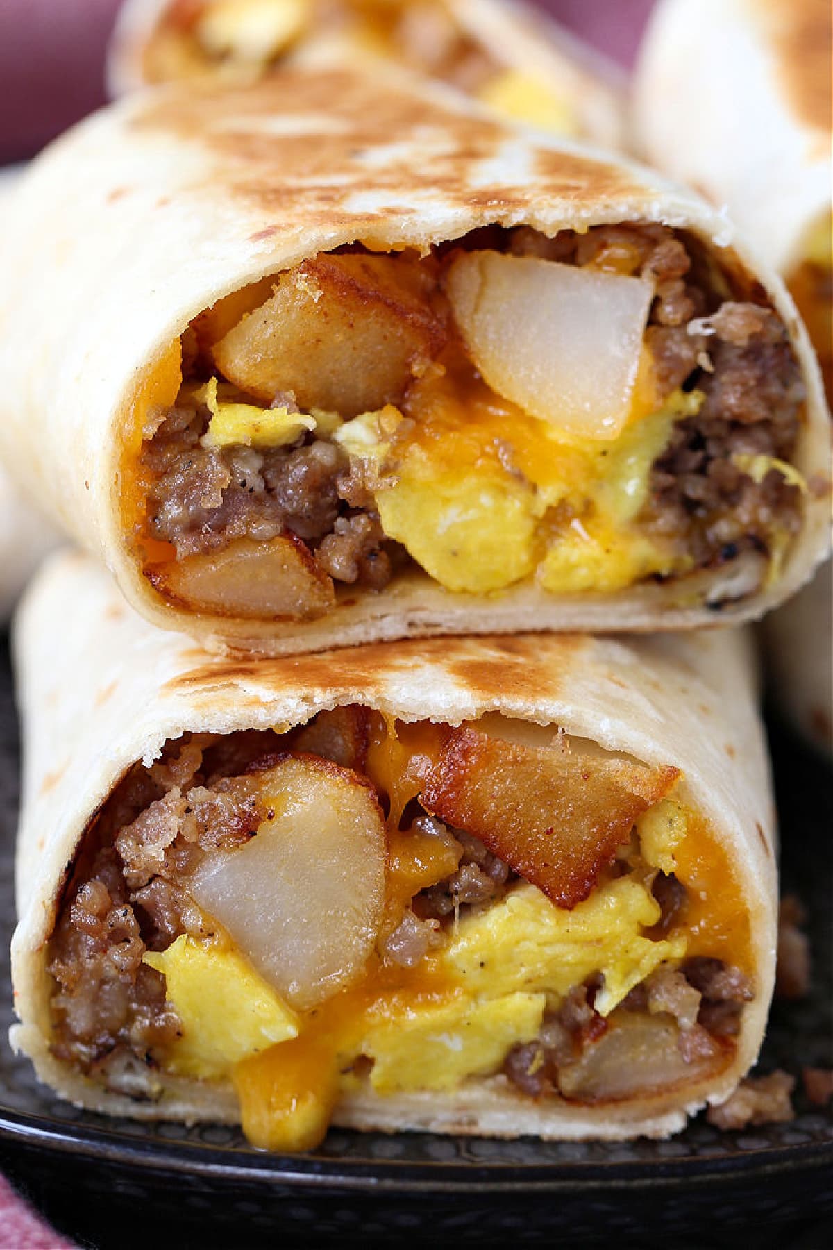 Breakfast Burritos with cheese, sausage, potatoes and egg cut in half on a plate