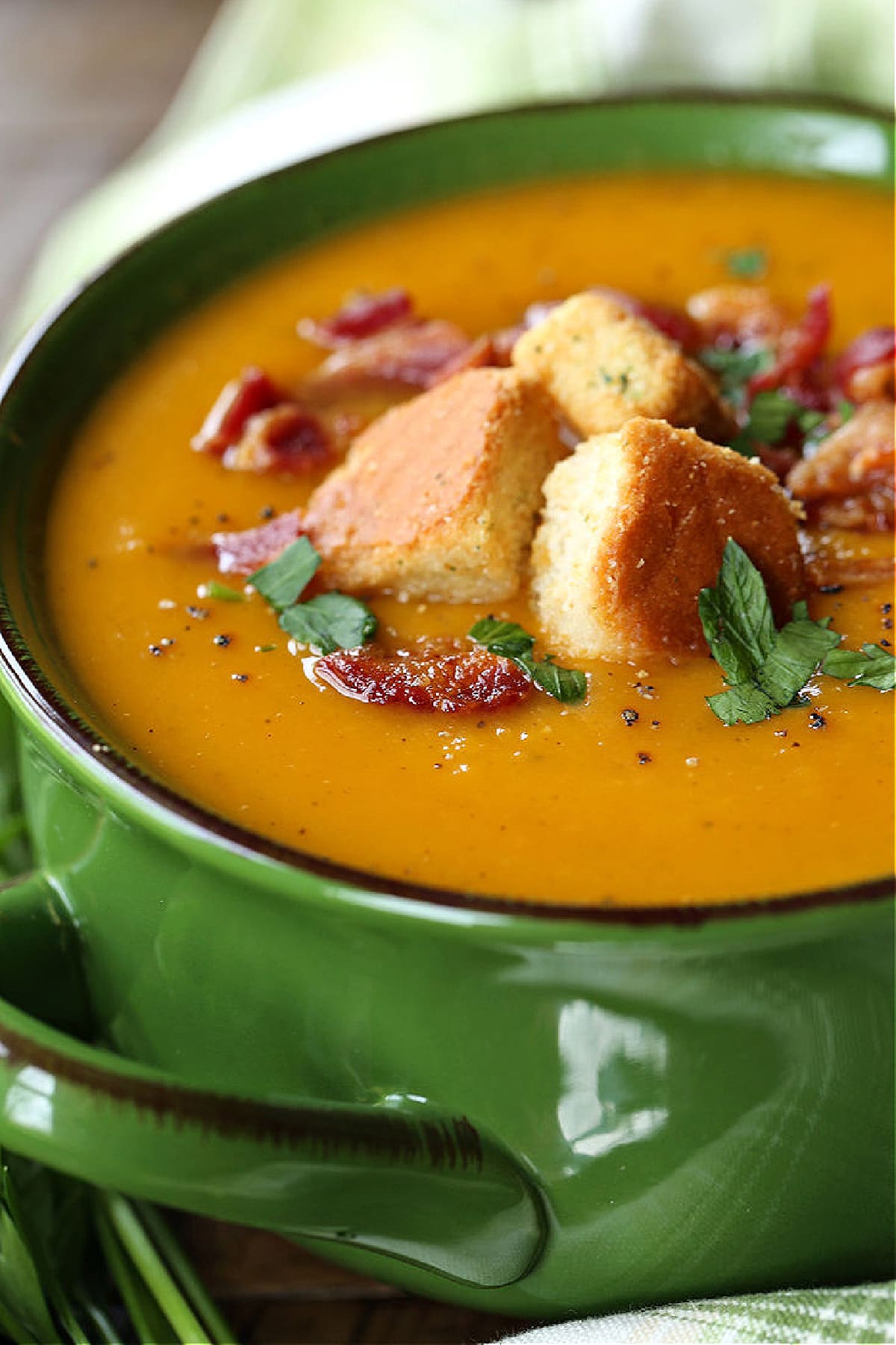 butternut squash soup in a green bowl with croutons and bacon