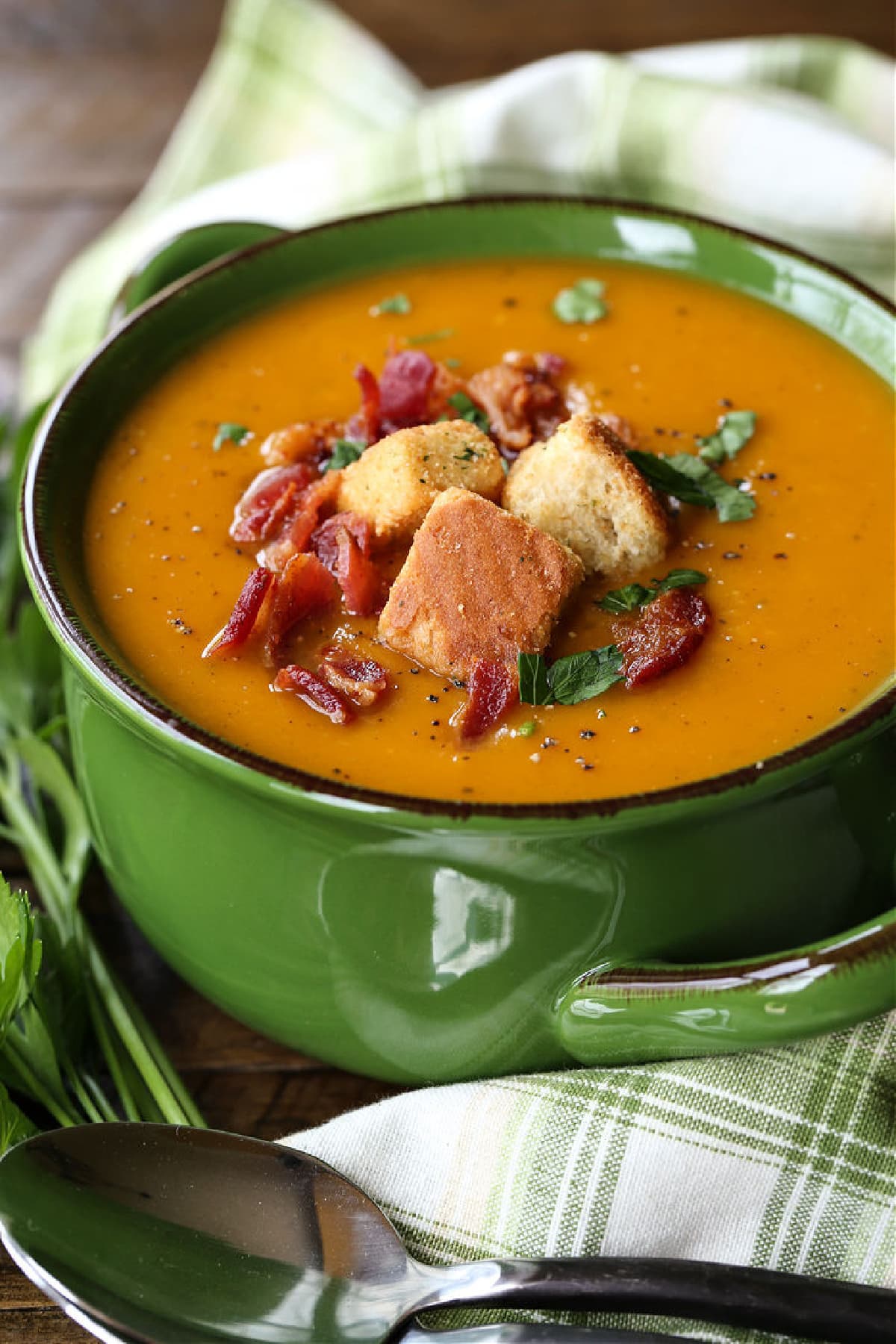 butternut squash soup in green crock with napkin and spoon on the side