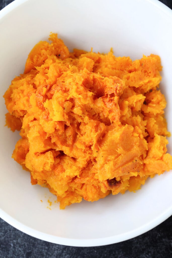 Filled with warm autumn spices, this smooth and creamy Roasted Butternut Squash Soup is the perfect comfort food to curl up with this fall. cooked, roasted squash in a white bowl