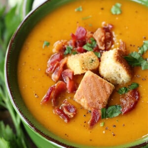 Roasted Butternut Squash Soup in a pot topped with bacon, parsley and croutons.