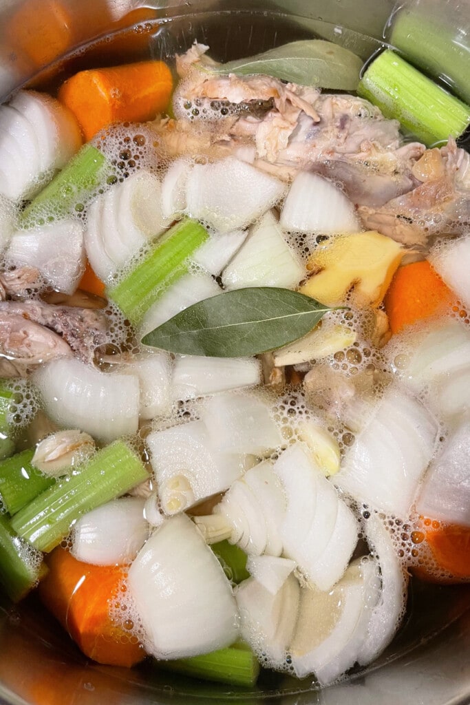 Rotisserie Chicken Stock is so easy to make with leftover rotisserie chicken bones! Use this hearty chicken stock in soups, stews and more! chicken bones and vegetables simmering in water for stock