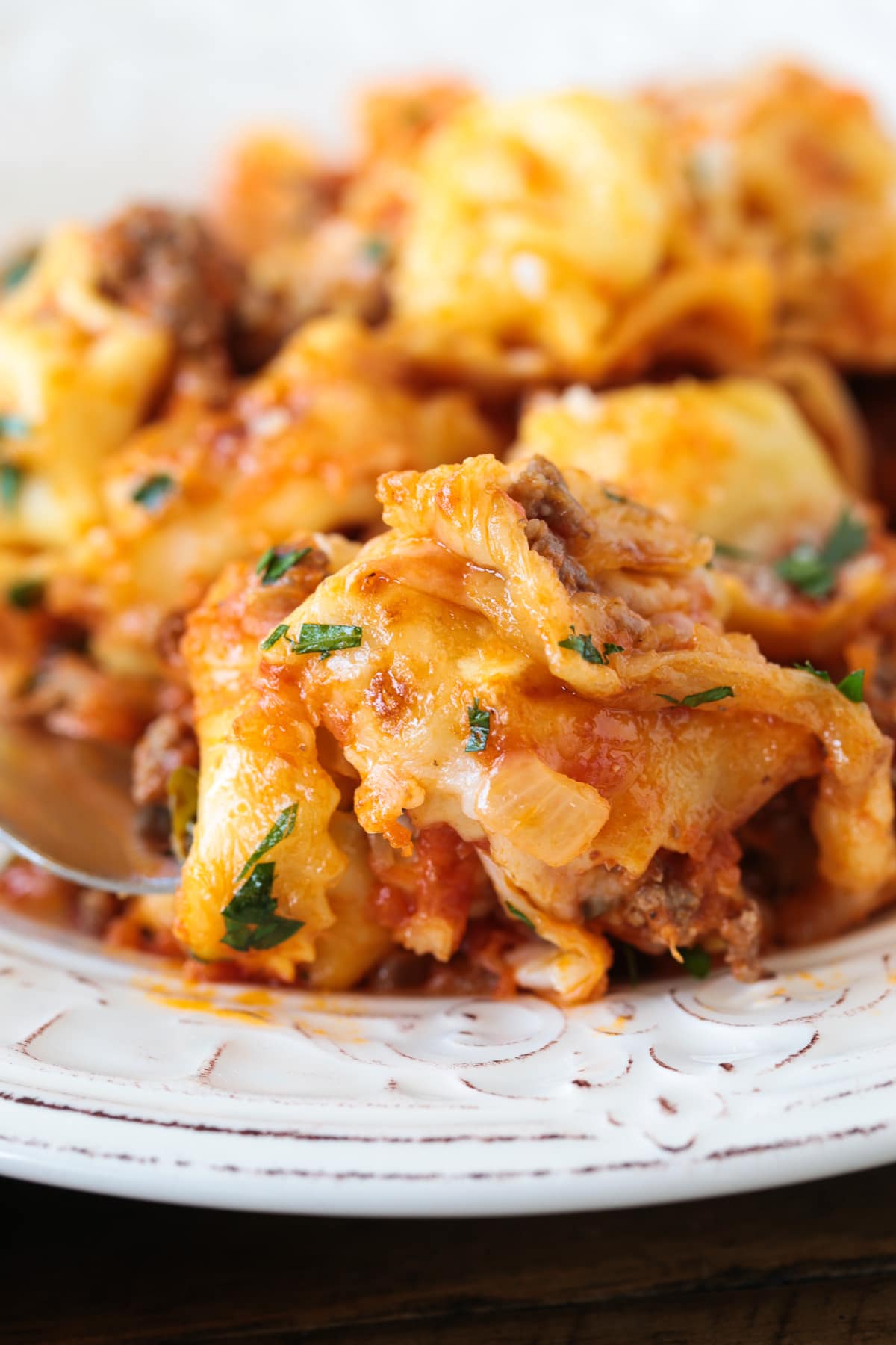 Make this Cheesy Tortellini Bake for an easy weeknight dinner or a cozy meal for guests. A hearty pasta casserole that everyone will love! forkful of tortellini bake on white plate