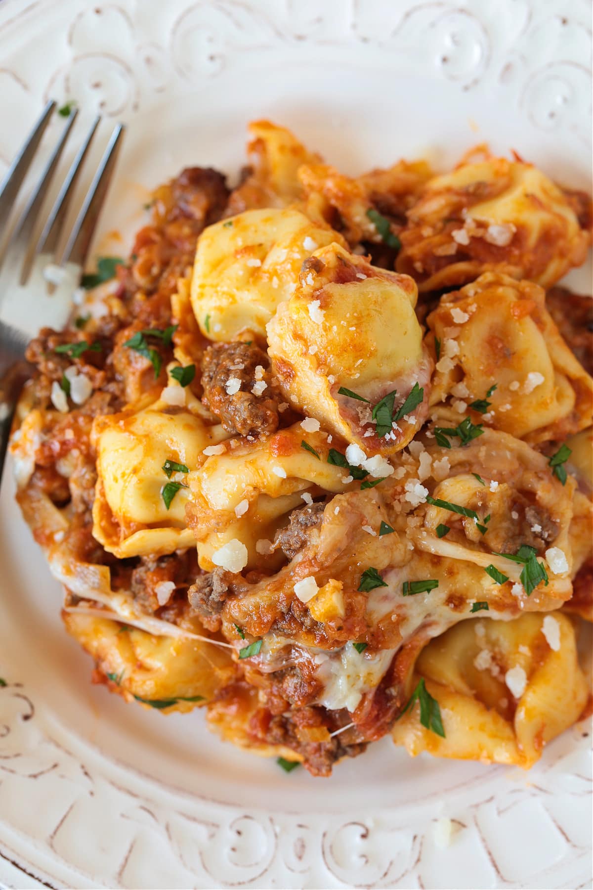 Make this Cheesy Tortellini Bake for an easy weeknight dinner or a cozy meal for guests. A hearty pasta casserole that everyone will love! cheese tortellini with ground beef and cheese on a plate with fork