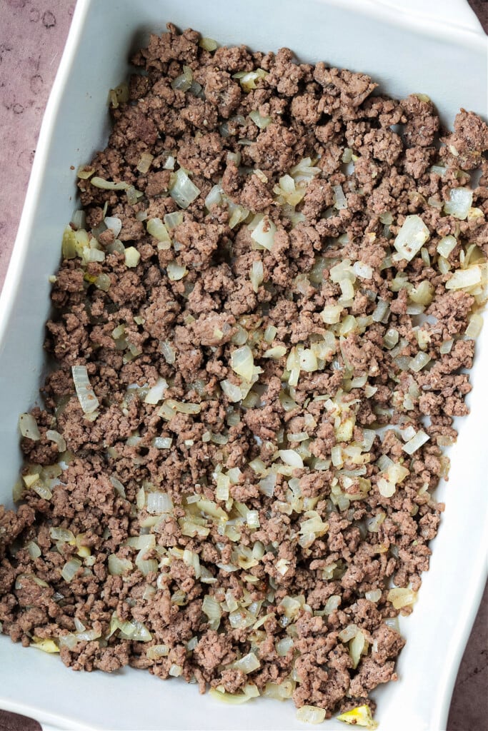 ground beef and onions in a white casserole dish