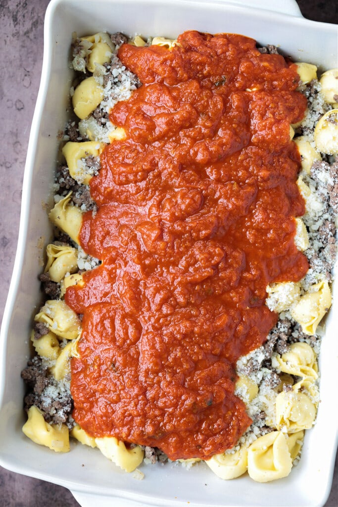 Make this Cheesy Tortellini Bake for an easy weeknight dinner or a cozy meal for guests. A hearty pasta casserole that everyone will love! marinara sauce on top of cheese tortellini and ground beef