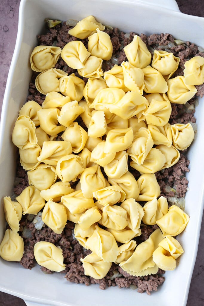 cheese tortellini layered on top of ground beef in a casserole dish