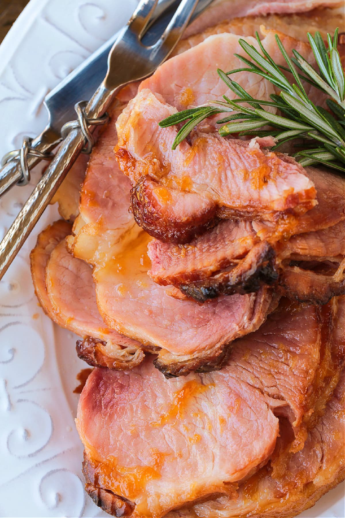 sliced, glazed ham on a serving platter with rosemary and serving fork
