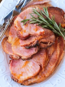 sliced ham on a platter with serving utensils and rosemary