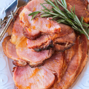 sliced ham on a platter with serving utensils and rosemary