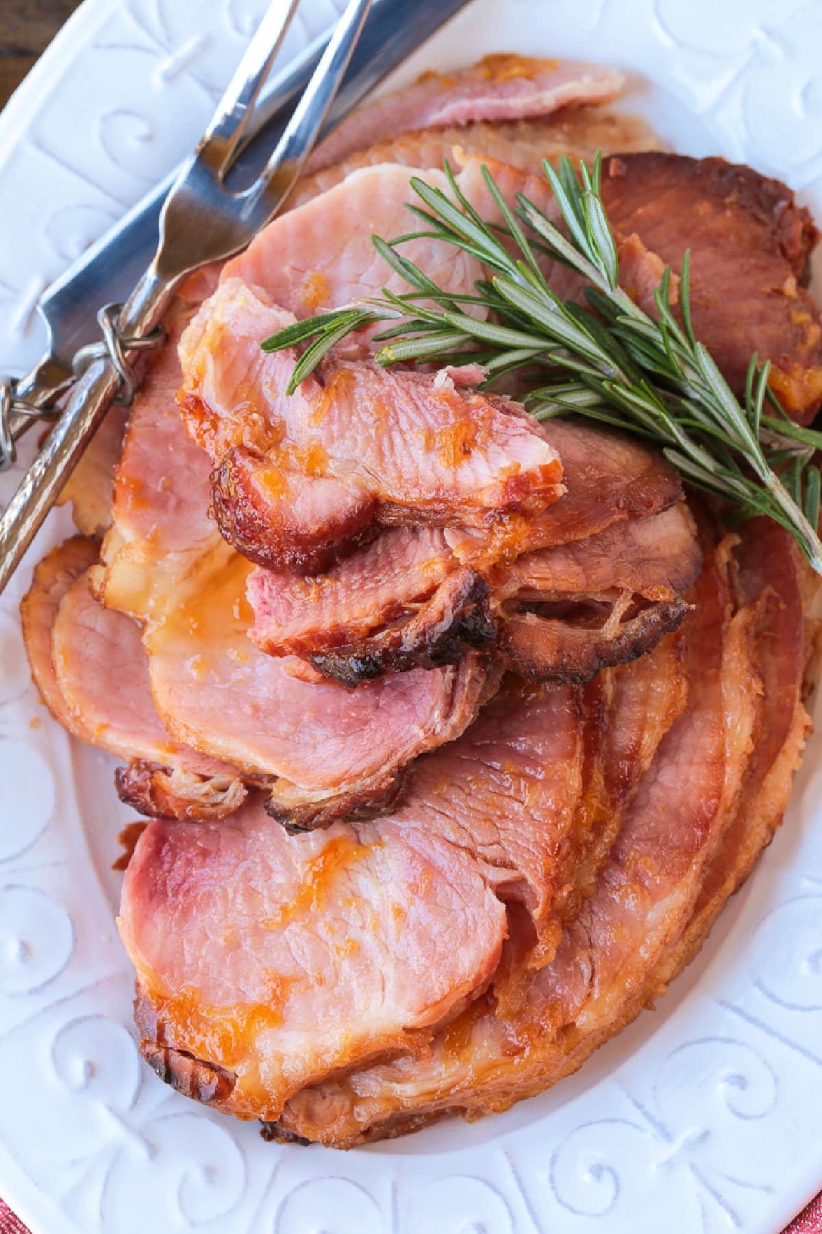 sliced ham on a platter with serving utensils and rosemary