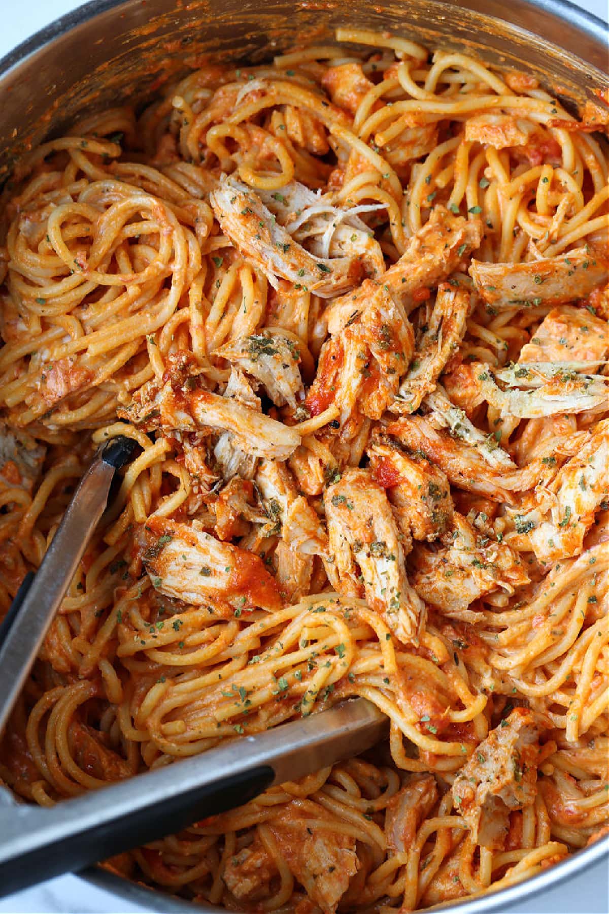 chicken spaghetti in a pot with tongs