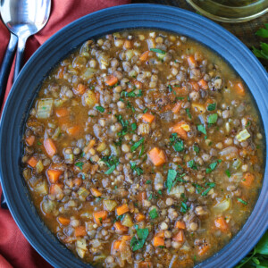 lentil soup in black bowl with napkin and spoons