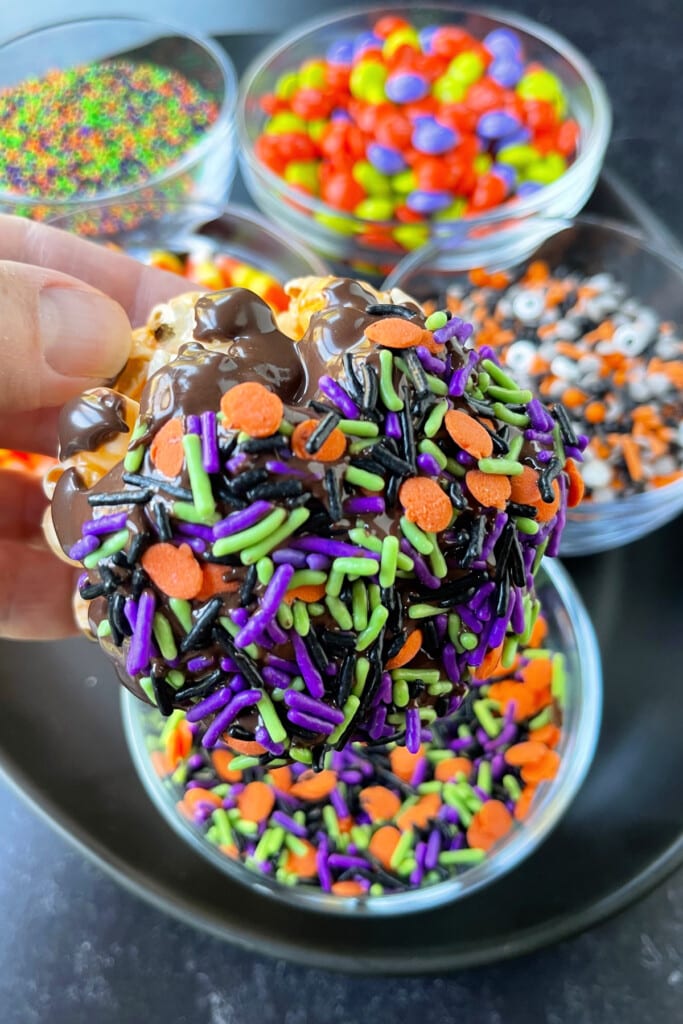 Halloween Popcorn Balls are a tasty and festive homemade treat for Halloween! Perfect for trick-or-treaters or for a Halloween party favor! popcorn balls dipped in sprinkles for Halloween
