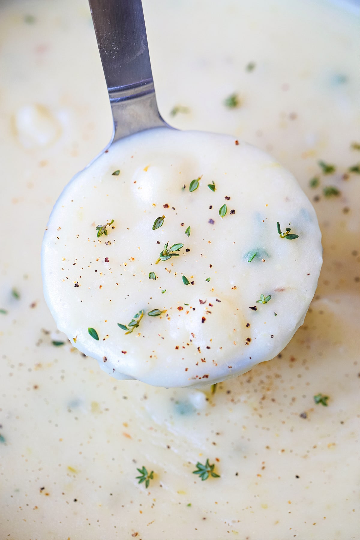 a ladle of potato soup with thyme and fresh pepper