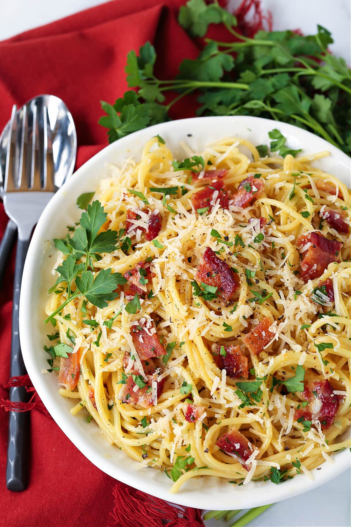 pasta carbonara in a white bowl with fork and napkin on the side