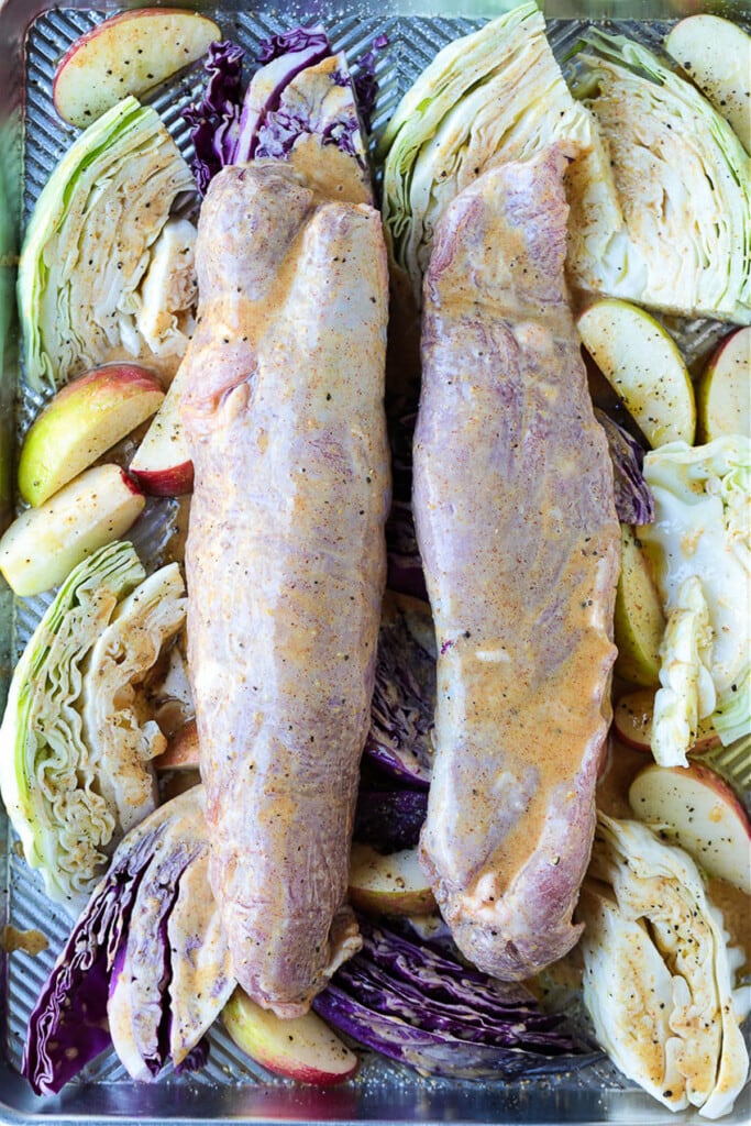 sauced pork tenderloins with apples and cabbage on a sheet pan