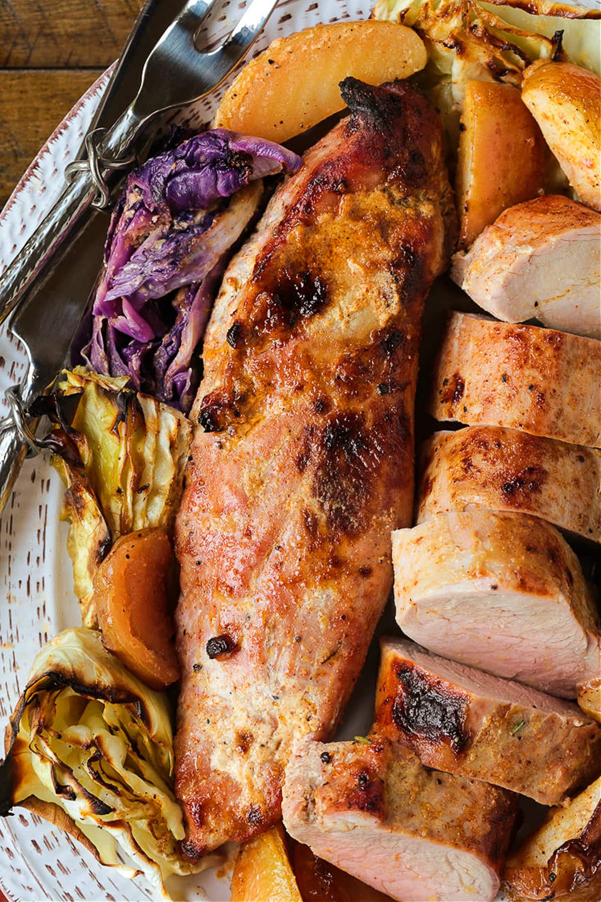 whole, roasted pork tenderloin on platter with cabbage and apple slices