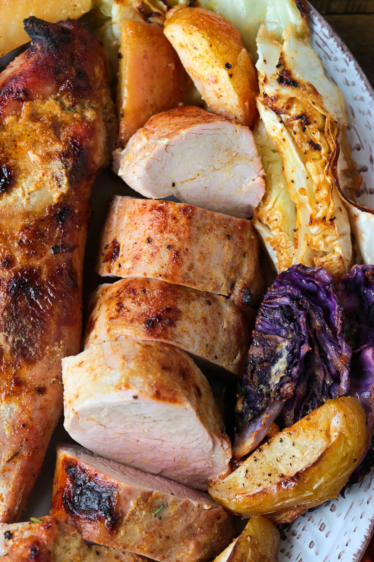 slices of pork tenderloin on a platter with cabbage and apple wedges