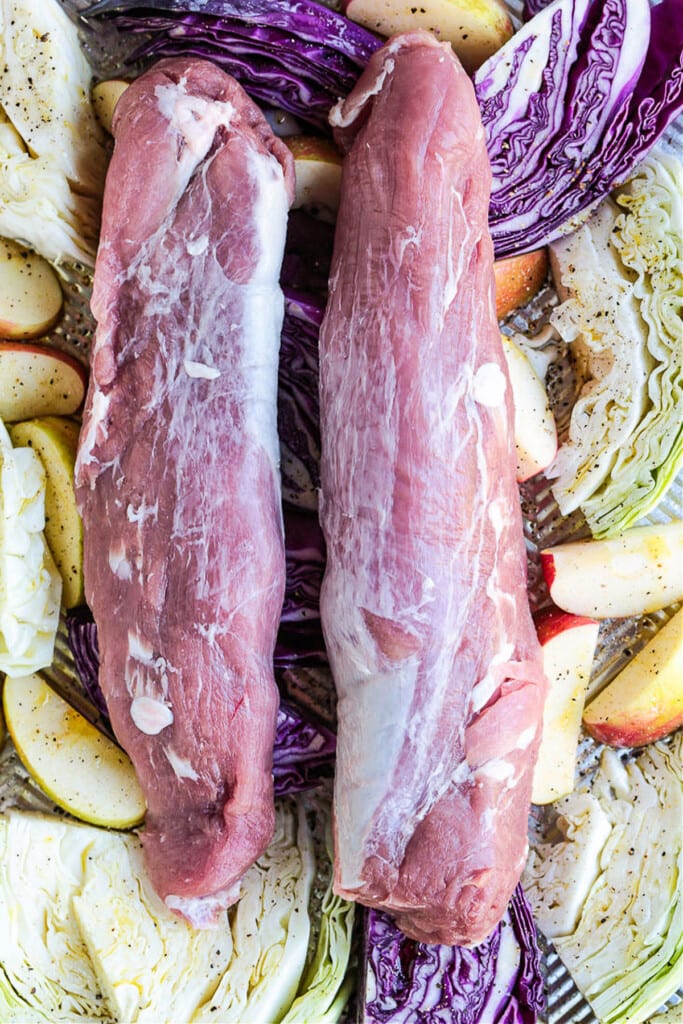 raw pork tenderloins on a sheet pan with apples and cabbage