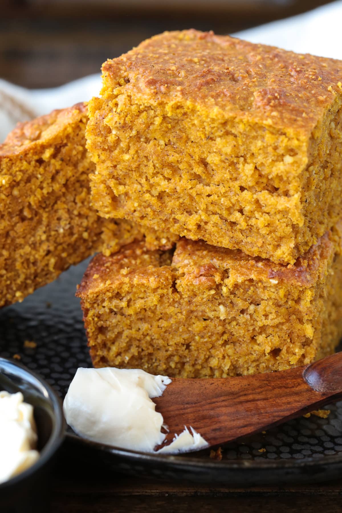 This Pumpkin Cornbread is giving all the fall vibes! Insanely moist and flavorful, with the perfect amount of pumpkin spice flavor! pumpkin cornbread stacked on a plate with a butter knife