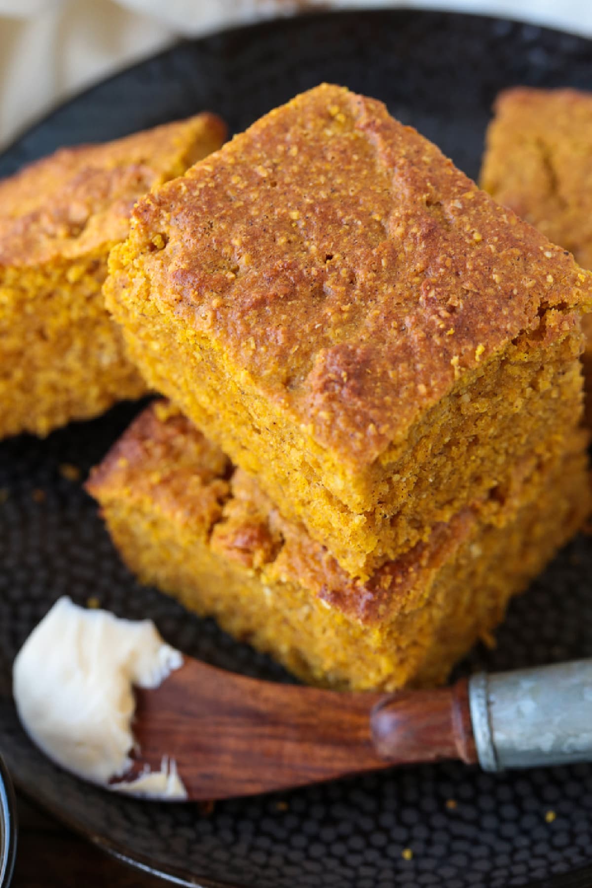 This Pumpkin Cornbread is giving all the fall vibes! Insanely moist and flavorful, with the perfect amount of pumpkin spice flavor! pumpkin cornbread stacked on plate with butter